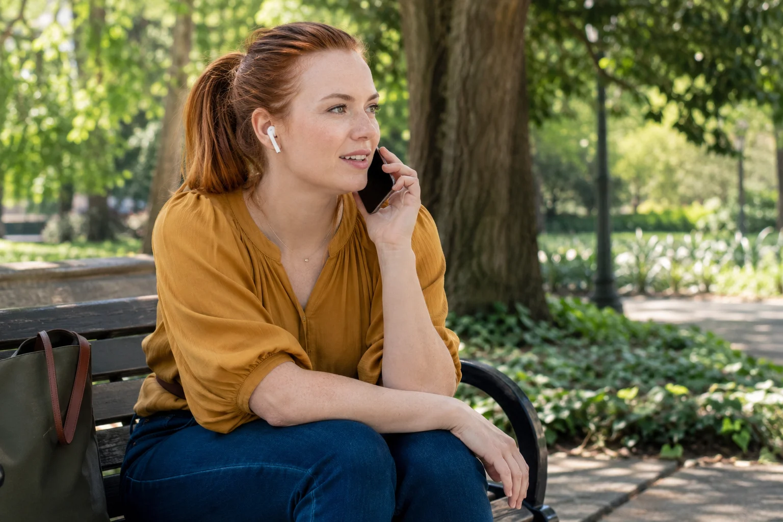 A woman wearing earbuds talking on a smartphone on a shaded park bench