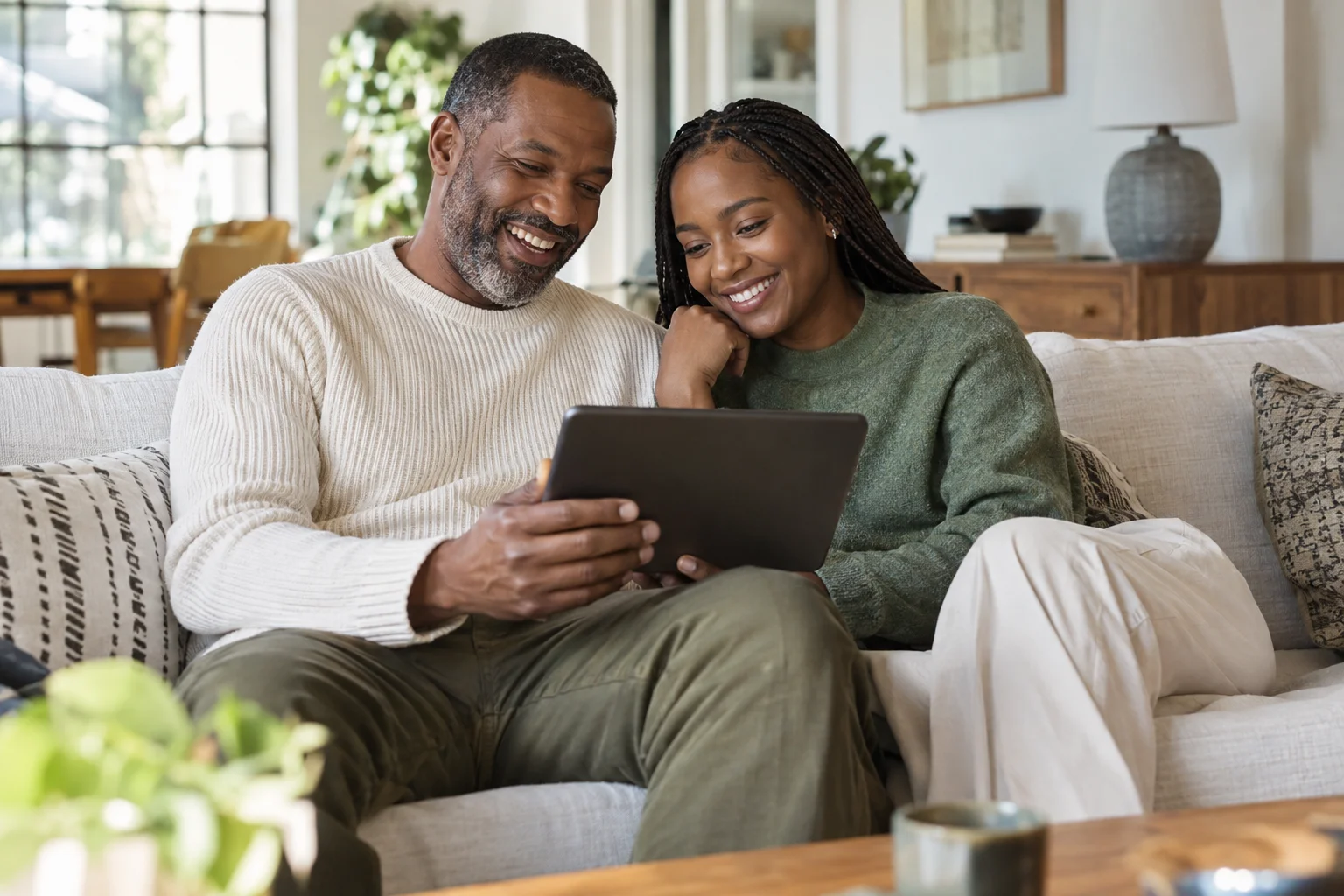 A couple smiling as they look at a tablet together on their sofa