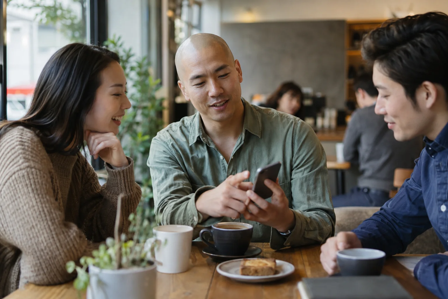 Three friends looking at a smartphone together at a café table